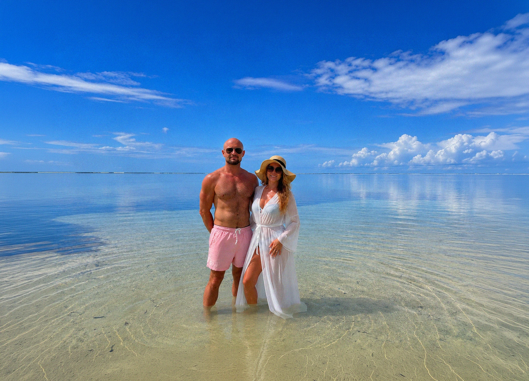 A couple standing in the shallow turquoise water of the tidal flats under a wide sky