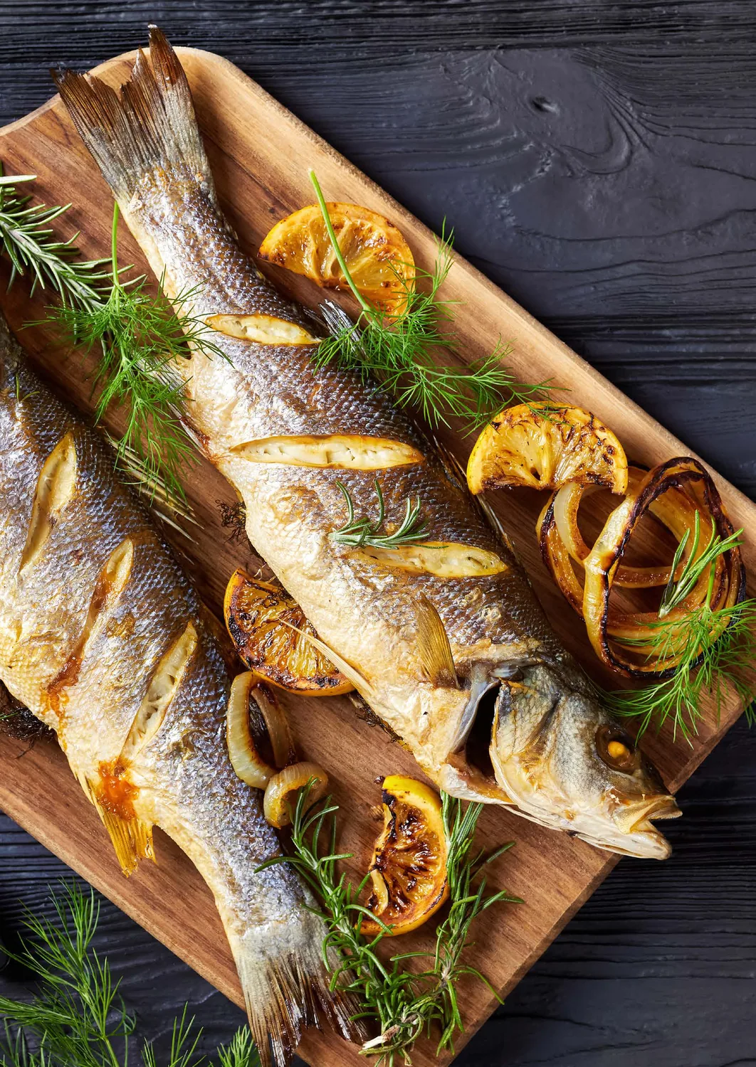 Whole grilled fish with herbs and citrus on a wooden board
